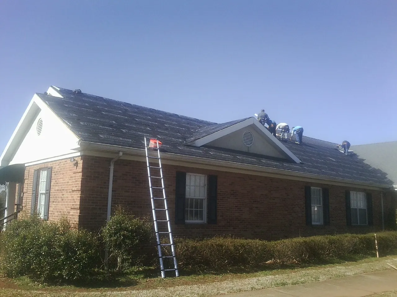 Crew tearing shingles off a brick ranch roof with a ladder set — Metal Roof Repair work by our crew in Herrin