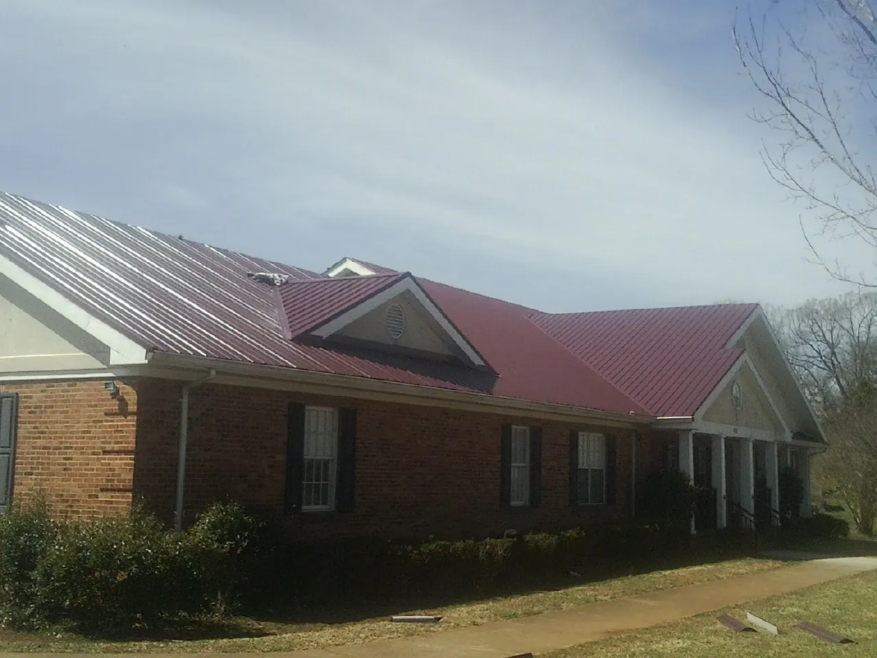 Red metal roof with gabled entries on a long brick building, from a Hail Damage Roof Repair job in Herrin