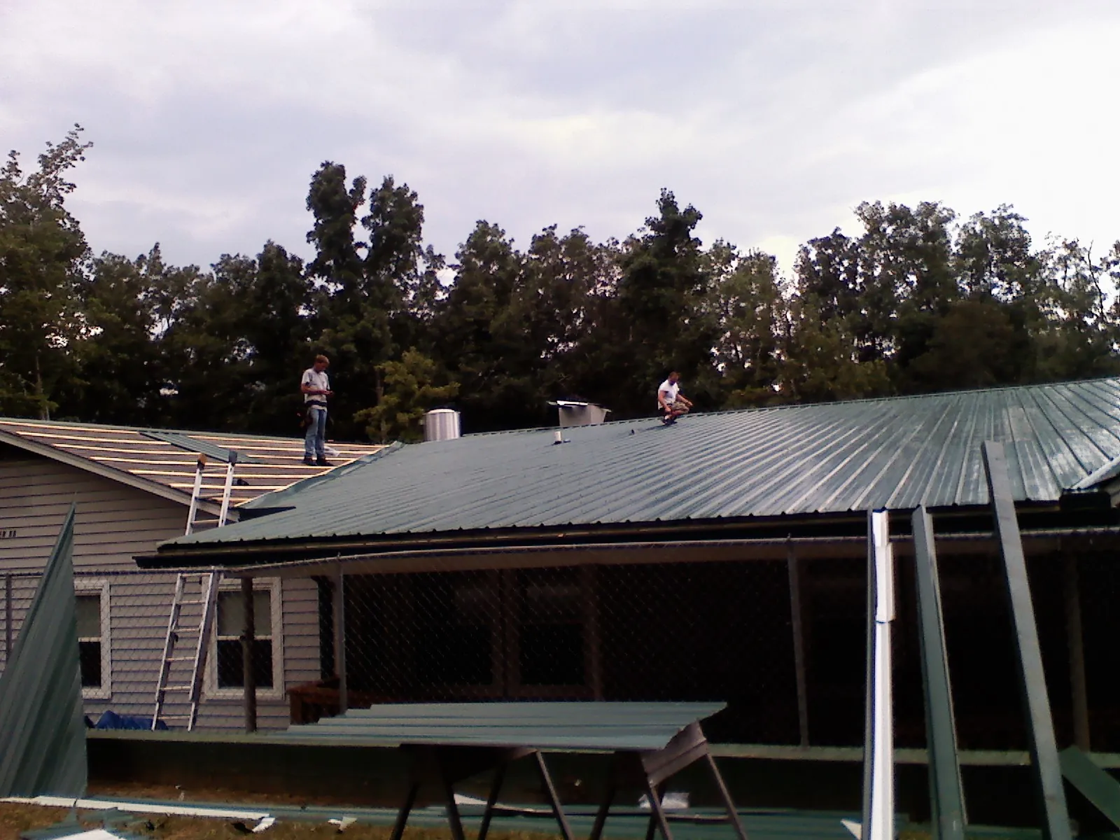 Two roofers installing green metal panels above a covered porch in Herrin