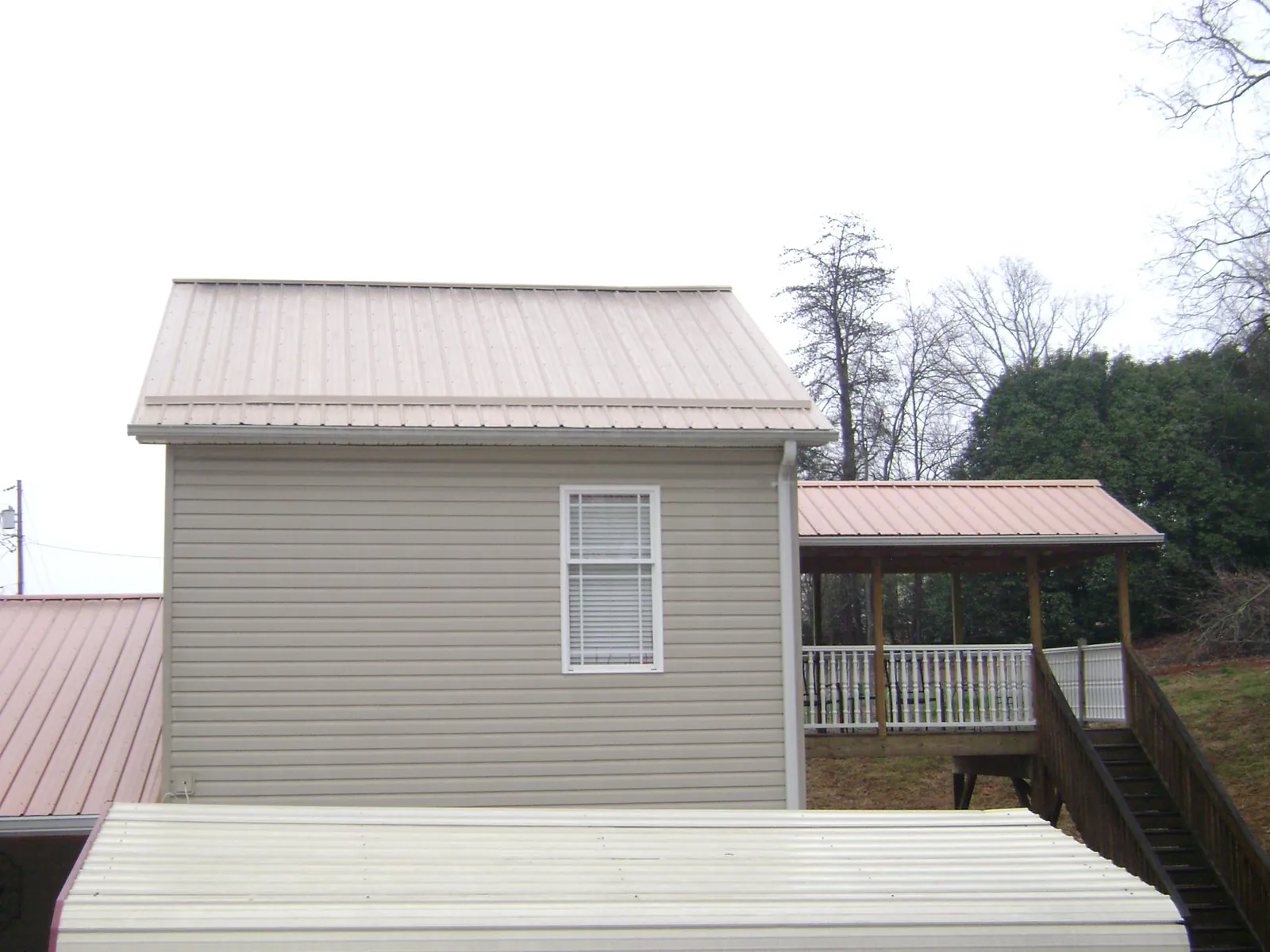 Tan metal roofs on a two story addition and attached porch, from a Roof Replacement job in Herrin